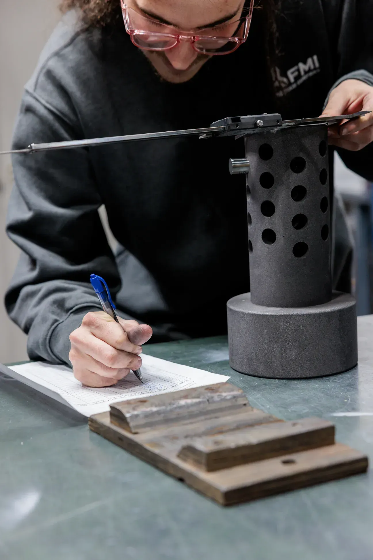 An FMI employee writing down measurements while balancing a ruler on a spherical metal component.