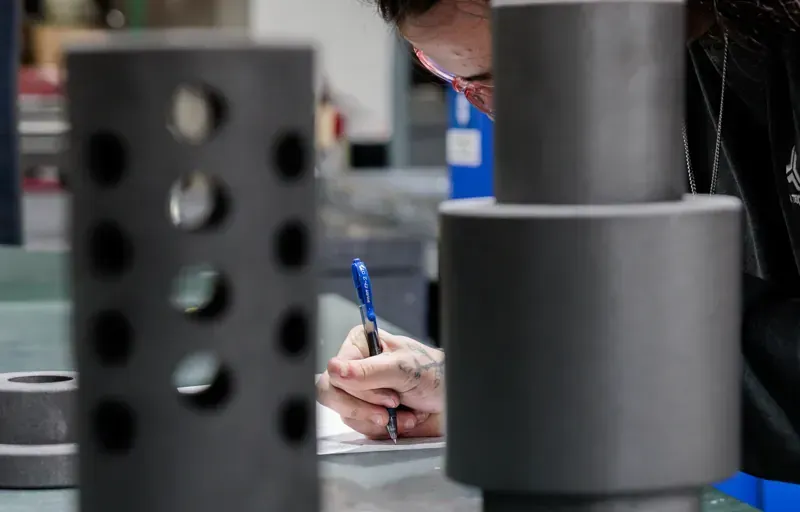 An FMI employee writing results on a table behind two metal cylinders.