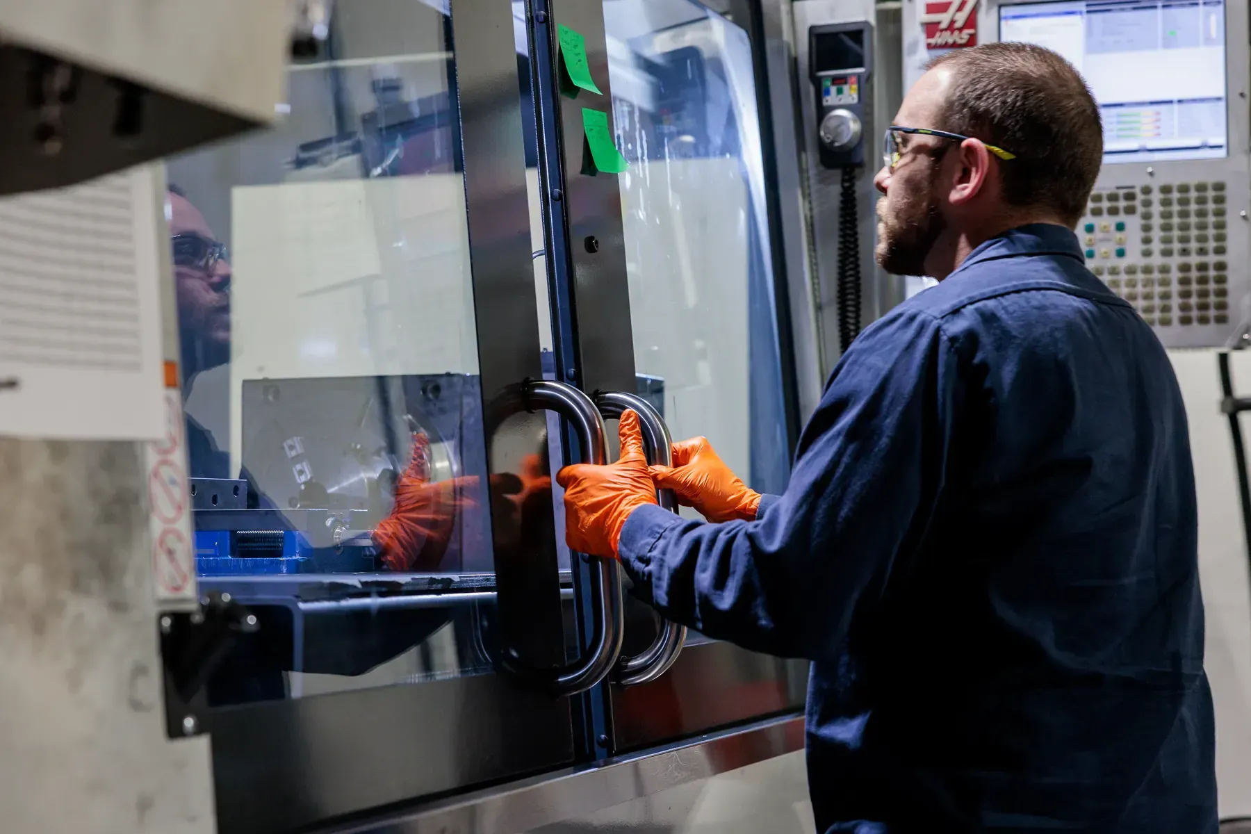 An FMI employee in full protective gear holding the handles of a closed door on a manufacturing machine.